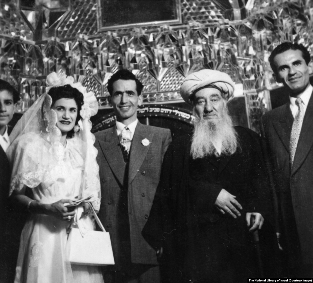 Jevrejsko vjenčanje na nepoznatoj lokaciji u Iranu 1950-ih godina. Ceremoniju vodi rabin Shlomo Cohen Tzedek (u sredini desno), glavni rabin u zemlji.Natpis na hebrejskom iza grupe odnosi se na stih iz Biblije: "Tvoja žena će biti kao rodna loza u tvojoj kući; tvoja djeca kao mladice masline oko tvoje trpeze".