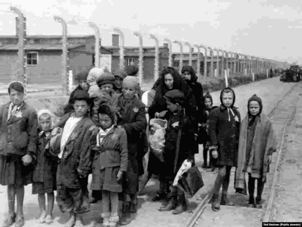 На фото справа: 1944 год. Женщина с детьми направляется в газовую камеру. На заднем фоне видны деревянные бараки – это лагеря Биркенау, дополнительно построенные в Освенциме. После войны здания были разрушены, но кирпичные стены и дымоходы сохранились.